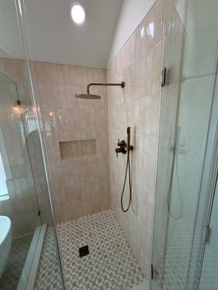 Frameless glass walk-in shower with brushed brass fixtures, a tiled niche and mosaic floor