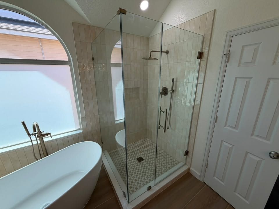 Soaking tub and frameless glass shower in front of an arched window