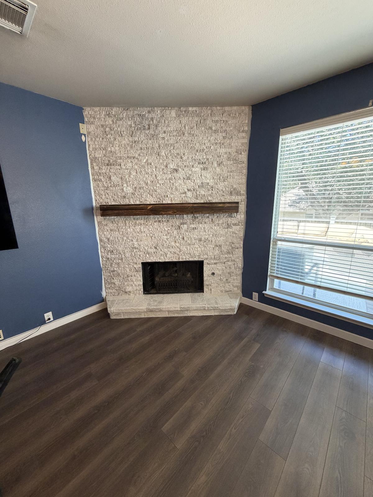 After: fireplace clad in stacked stone to the ceiling with a rustic wood beam mantel