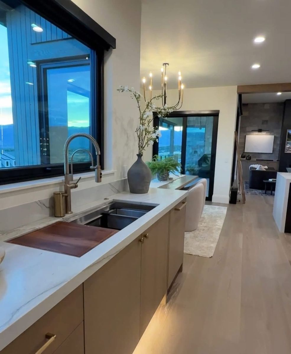 Kitchen counter with a workstation sink, brass pull-down faucet, wood-tone cabinets and under-cabinet lighting