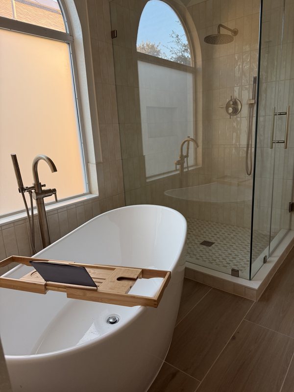 Freestanding white soaking tub with a wood bath tray and floor-mount filler next to a frameless glass shower