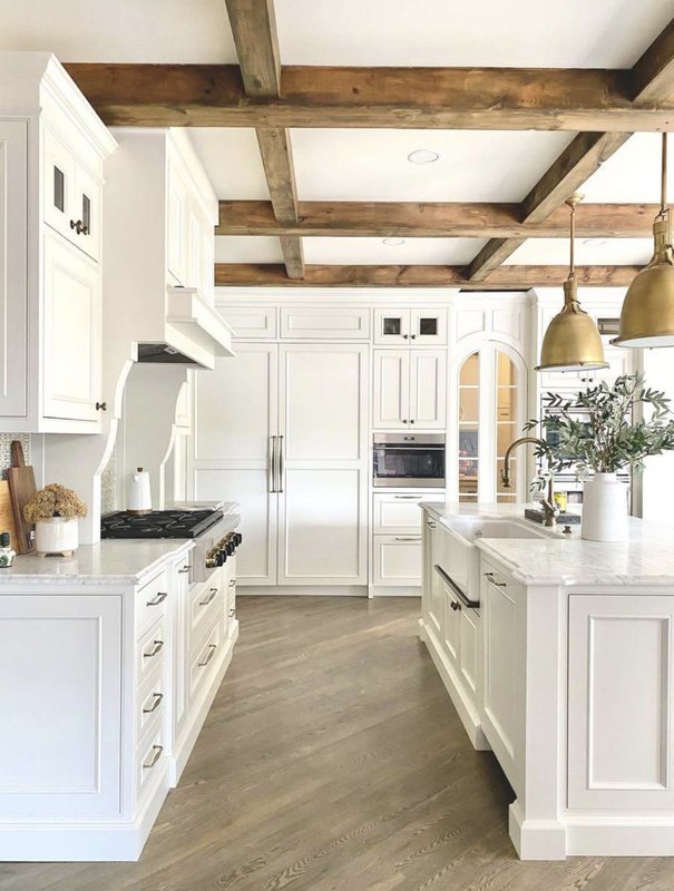 White kitchen with exposed wood ceiling beams, lantern pendants and a long island