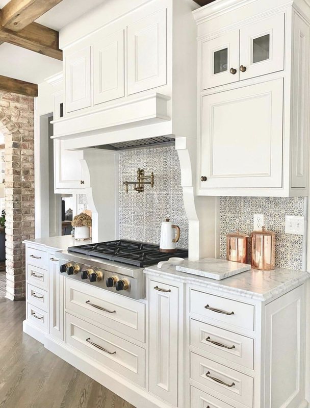White shaker kitchen with a custom range hood, professional range and marble-look backsplash
