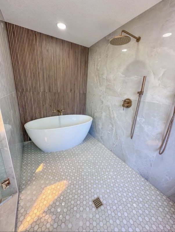 Freestanding soaking tub against a wood slat accent wall beside a glass shower with brass fixtures
