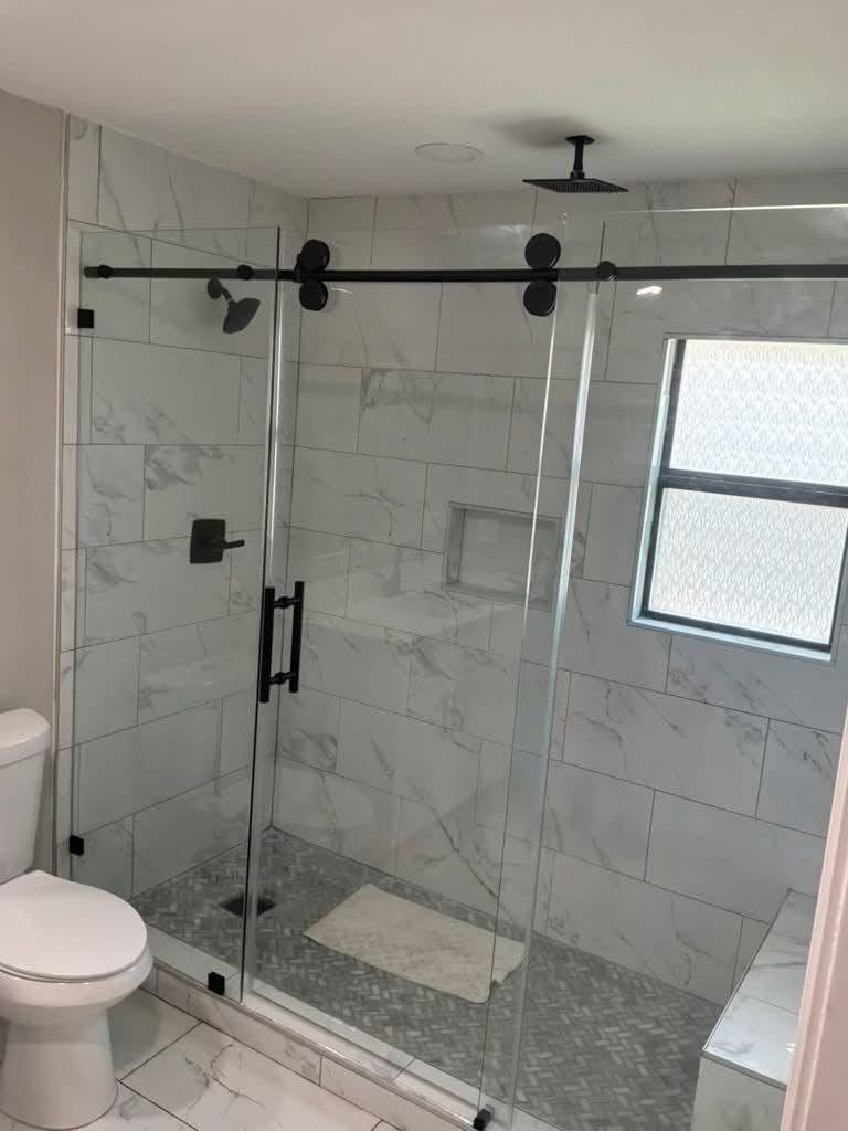 Marble-look tile shower with a sliding glass door on matte black hardware, a recessed niche and herringbone mosaic floor